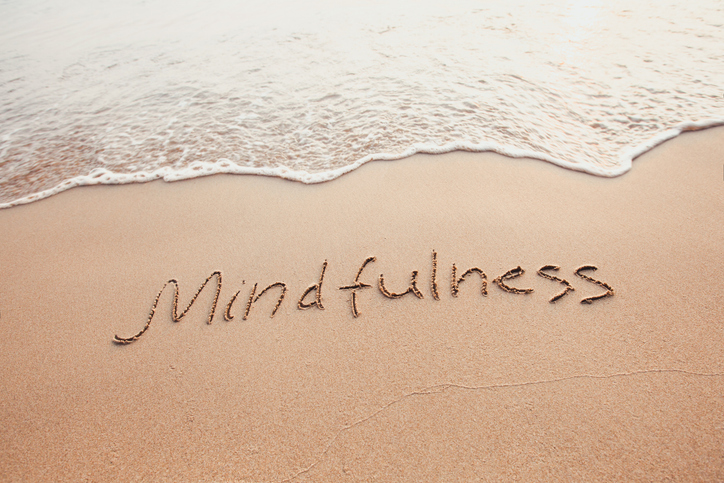 Das Wort „Mindfulness“ in Sand geschrieben, eine Welle läuft heran