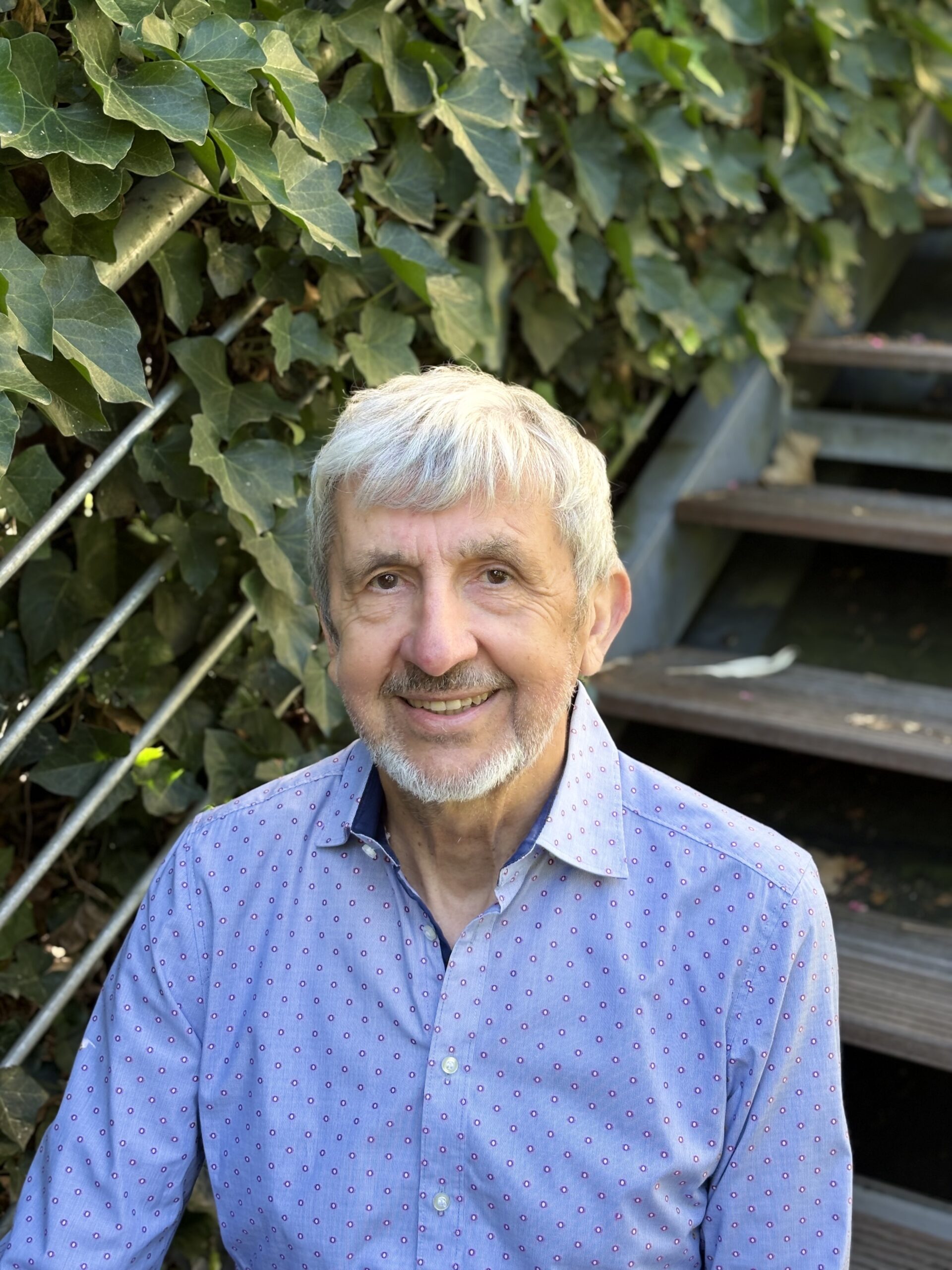Reinhard Allgaier sitzt in blauem Hemd auf einer Treppe vor einer Efeuwand